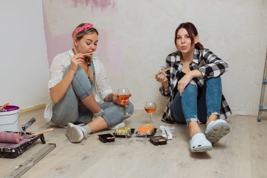 Two girlfriends cute girls eat sushi after working with the repair of the room. The LGBT family is renovating the room. Painters' lunch.