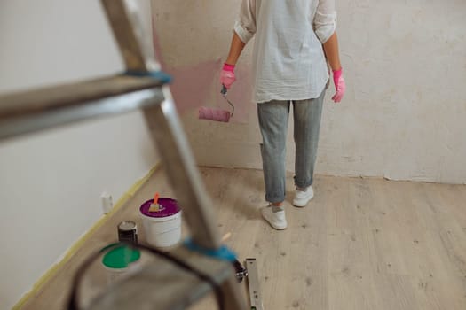 Young woman with the roller painting the wall in new house.