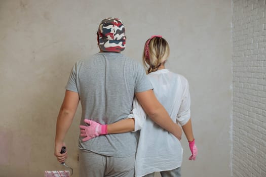 A happy young family makes a dream repair inside the house with their own hands. Husband and wife paint the wall in the room.