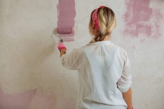 Young woman with the roller painting the wall in new house.