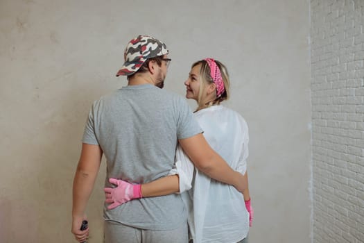 A happy young family makes a dream repair inside the house with their own hands. Husband and wife paint the wall in the room.