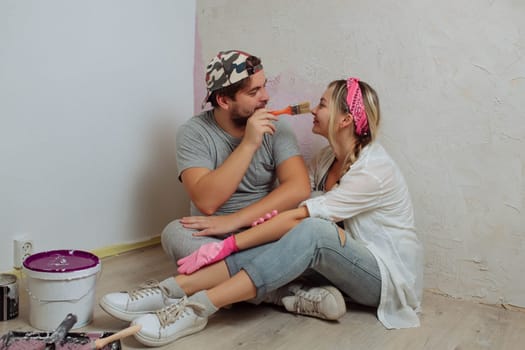 A happy young family makes a dream repair inside the house with their own hands. Husband and wife paint the wall in the room.