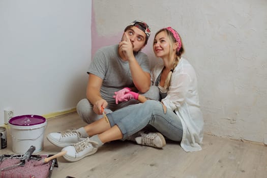 A happy young family makes a dream repair inside the house with their own hands. Husband and wife paint the wall in the room.