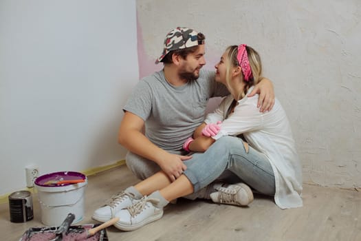 A happy young family makes a dream repair inside the house with their own hands. Husband and wife paint the wall in the room.