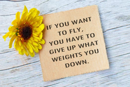 Motivational quote on torn brown paper on wooden surface with sunflowers. If you want to fly, you have to give up what weights you down.