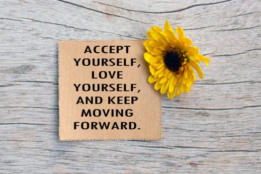 Motivational quote on torn brown paper on wooden surface with sunflowers. Accept yourself, Love yourself, and keep moving forward.