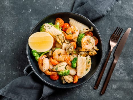 Mixed Seafood Contain Shrimps, Mussels, Calamari Squids and Fish with Broccoli, Cherry Tomato, Lemon on Black dish in restaurant-style platting. Seafood salad on dark background. Top view