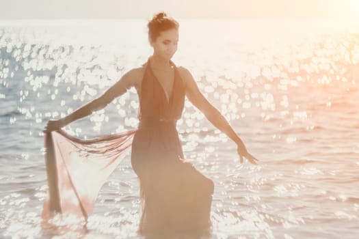 Side view a Young beautiful sensual woman in a red long dress posing on a rock high above the sea during sunrise. Girl on the nature on blue sky background. Fashion photo.