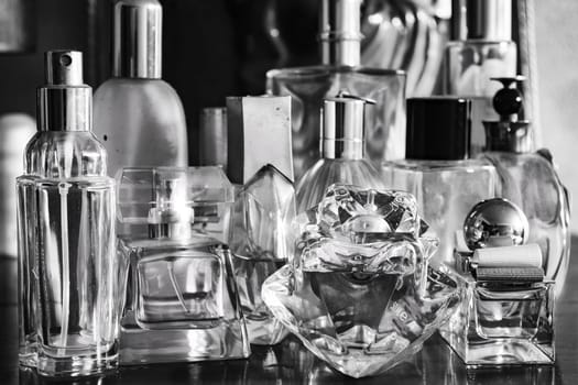 black and white perfume bottles, some full and some empty, lined up on a wooden sideboard