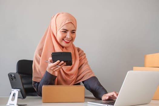 Asian Muslim businesswoman checks stock orders and saves them on her home office laptop. small business owner Shipping in online markets The concept of freedom in life.