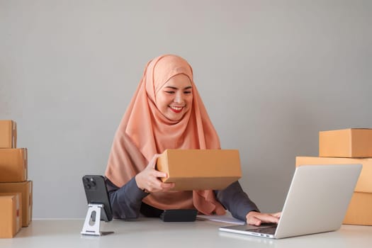 Asian Muslim businesswoman checks stock orders and saves them on her home office laptop. small business owner Shipping in online markets The concept of freedom in life.