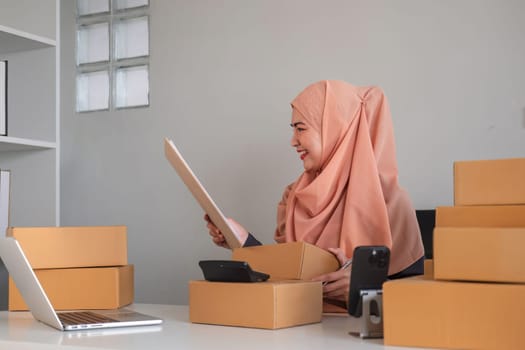 Asian Muslim businesswoman checks stock orders and saves them on her home office laptop. small business owner Shipping in online markets The concept of freedom in life.