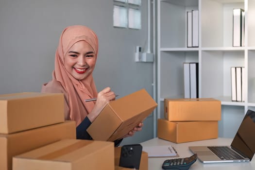 Asian Muslim businesswoman checks stock orders and saves them on her home office laptop. small business owner Shipping in online markets The concept of freedom in life.