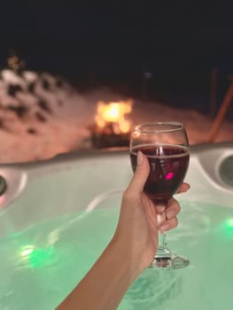 A woman's hand holds a glass of red wine on the background of a jacuzzi. High quality photo