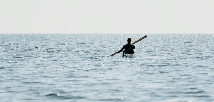 Happy smiling woman in kayak on ocean, paddling with wooden oar. Calm sea water and horizon in background