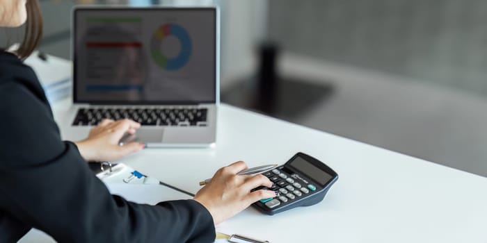 Businesswoman using a calculator to calculate numbers on a company's financial documents, she is analyzing historical financial data to plan how to grow the company. Financial concept..