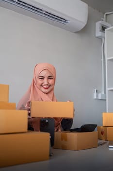 Muslim women selling online at home with box. Selling online with box to accept order from customer. SME business idea. Parcel delivery. muslim woman working smartphone and laptop at home.