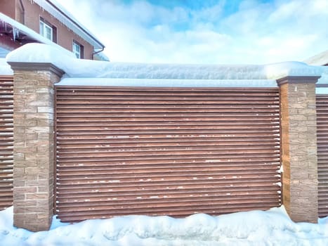 Fence section with metal or wood planks, blinds and brick columns in winter snow. Background, texture, pattern, frame, place for text and copy space