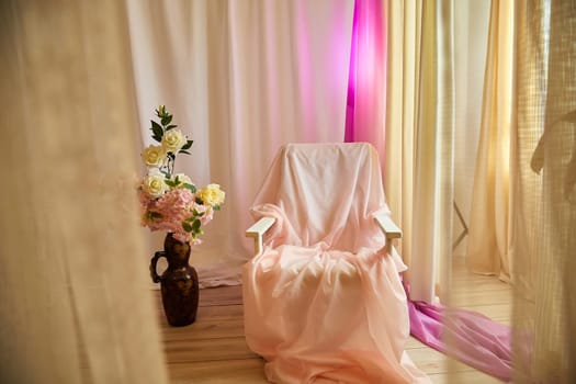 Delicate pink bright interior of the room with an armchair, vase with roses, draped curtains and a window. Location and background in the photo studio