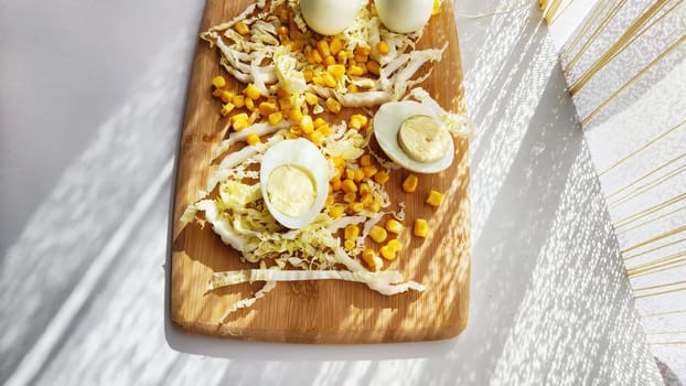 Chopped Peking cabbage, peeled eggs and yellow canned corn on cutting board as background. Cooking a healthy eco-friendly salad from natural products. Copy space and place for text