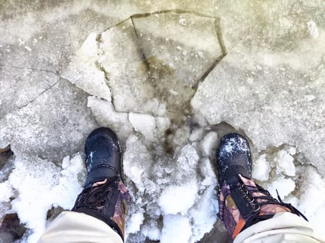 Feet of Hunter or fisherman in big warm boots on winter day on snow. Top view. Fisherman on the ice of a river, lake, reservoir on spring day with melting ice. Dangerous fishing in autumn