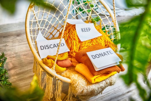 Signs with the words keep, donate, discard and fashion clothes folded in stacks in cozy room. The concept of cluttering and decluttering. Background