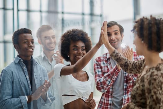 Excited multiracial employees give high five engaged in teambuilding activity in office together