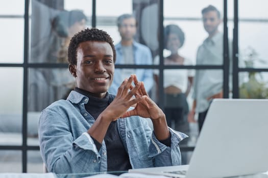 smiling leader business man with executives working on laptop in background.