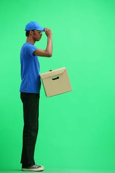 A male deliveryman, on a green background, full-length, with a box.