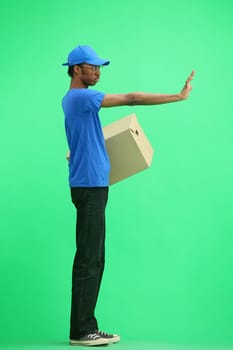 A male deliveryman, on a green background, in full height, with a box, shows a stop sign.