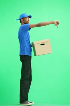 A male deliveryman, on a green background, full-length, with a box, shows his finger down.