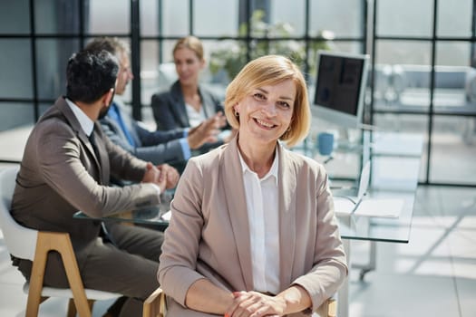 female boss against the background of her colleagues looks at the camera in a modern office