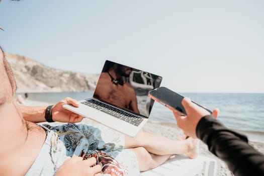 Digital nomad, Business man working on laptop by the sea. Man typing on computer by the sea at sunset, makes a business transaction online from a distance. Freelance, remote work on vacation