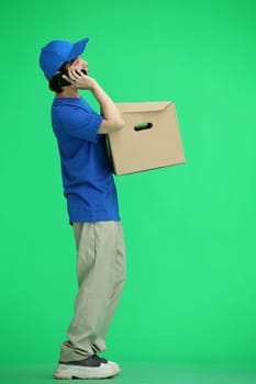 The delivery guy, on a green background, full-length, with a box and a phone.