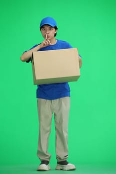 The delivery guy, on a green background, full-length, with a box, shows a sign of silence.