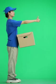 The delivery guy, on a green background, full-length, with a box, shows his finger up.