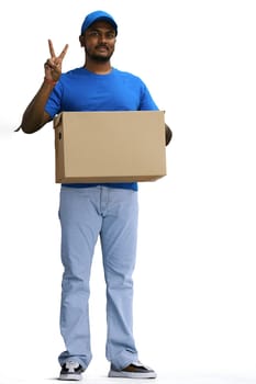 A male deliveryman with a box, on a white background, in full height, shows a victory sign.