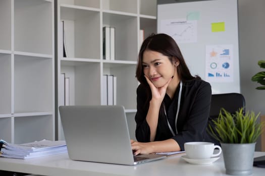 Portrait of young Asian woman working on laptop in modern office Perform accounting analysis, report investment data. Financial concepts and tax system.