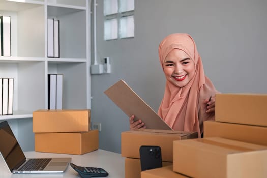 Asian Muslim businesswoman checks stock orders and saves them on her home office laptop. small business owner Shipping in online markets The concept of freedom in life.