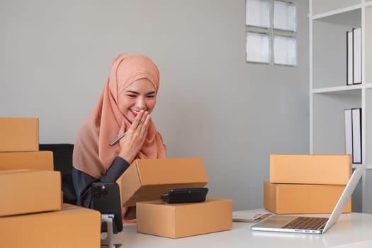 Asian Muslim businesswoman checks stock orders and saves them on her home office laptop. small business owner Shipping in online markets The concept of freedom in life.