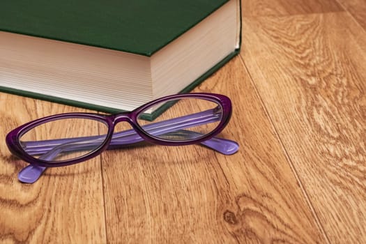 Glasses and a green thick book on a wooden table