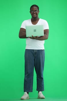 Full-length man in a white T-shirt typing on a laptop on a green background.