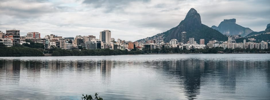 "Sisters pose at Pedra da Gavea with a lagoon and city view beneath a cloudy sky."