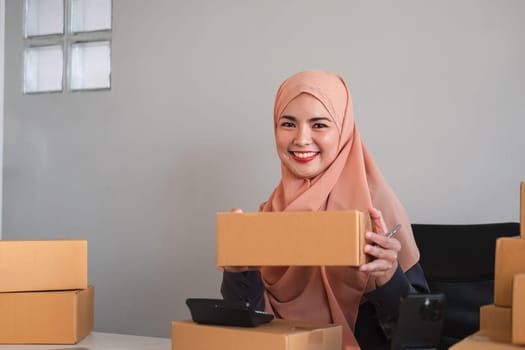 Portrait of a small business startup, SME owner, female entrepreneur, working, checking orders online. To prepare to pack boxes for sale to SME customers online business ideas.