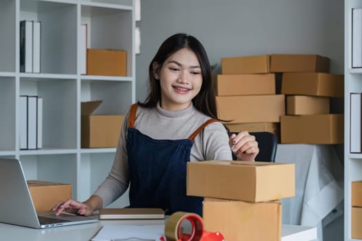 Startup SME small business entrepreneur SME or freelance Asian woman using a laptop with box, online marketing packaging box and delivery, SME concept..