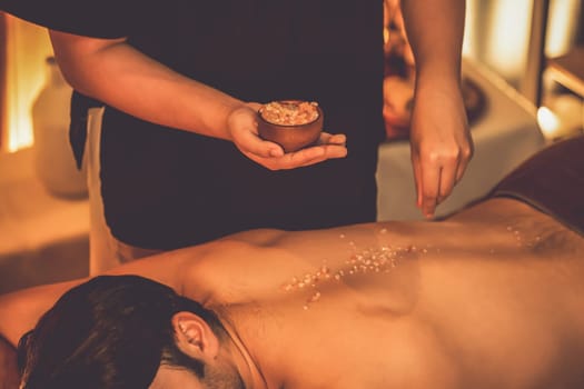 Man customer having exfoliation treatment in luxury spa salon with warmth candle light ambient. Salt scrub beauty treatment in Health spa body scrub. Quiescent