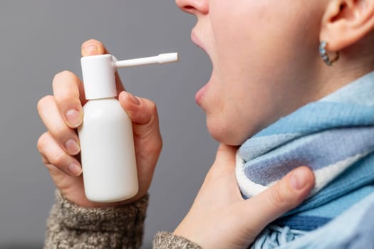 A woman with a sore throat sprays medicine aerosol spray down her throat. Disease prevention.