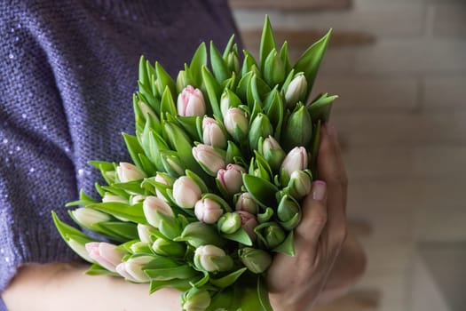 Young beautiful woman holding a spring bouquet of yellow tulips in her hand. Bunch of fresh cut spring flowers in female hands