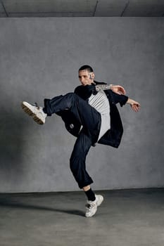 Graceful performer with tattooed body, earrings, beard. Dressed in white t-shirt and sneakers, black denim shirt and pants. Dancing on gray background. Dancehall, hip-hop. Full length, copy space