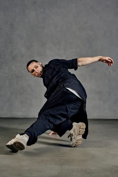 Flexible male with tattooed body and face, earrings, beard. Dressed in white t-shirt and sneakers, black denim shirt, pants. Dancing on gray background. Dancehall, hip-hop. Full length, copy space